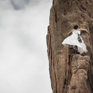 Frau im weissen Kleid hält sich beim Klettern an Fels fest
